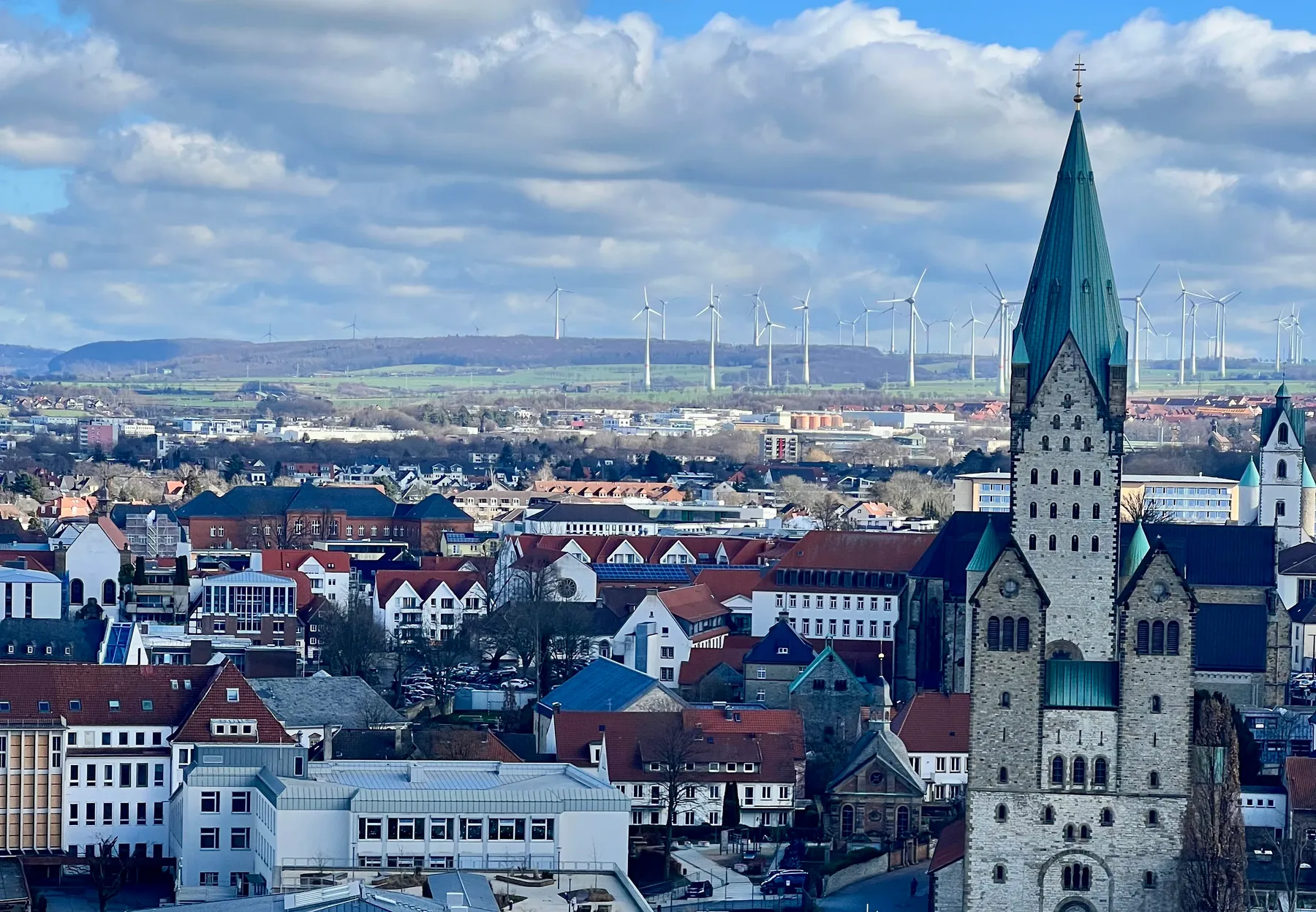 Blick über die Dächer von Paderborn: der Dom mit seinem grünen Turmhelm, dahinter die Windräder auf der Paderborner Hochfläche