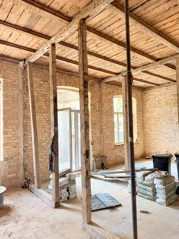 Entkerntes Obergeschoss eines Altbaus: freigelegte Ziegelwände, Holzbalkendecke und Stützen, im Hintergrund neue Fenster