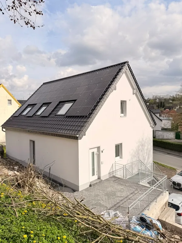 Fertiges Wohnhaus nach der Sanierung: heller Putz, neue Fenster, Photovoltaik auf dem Dach, gepflasterte Terrasse