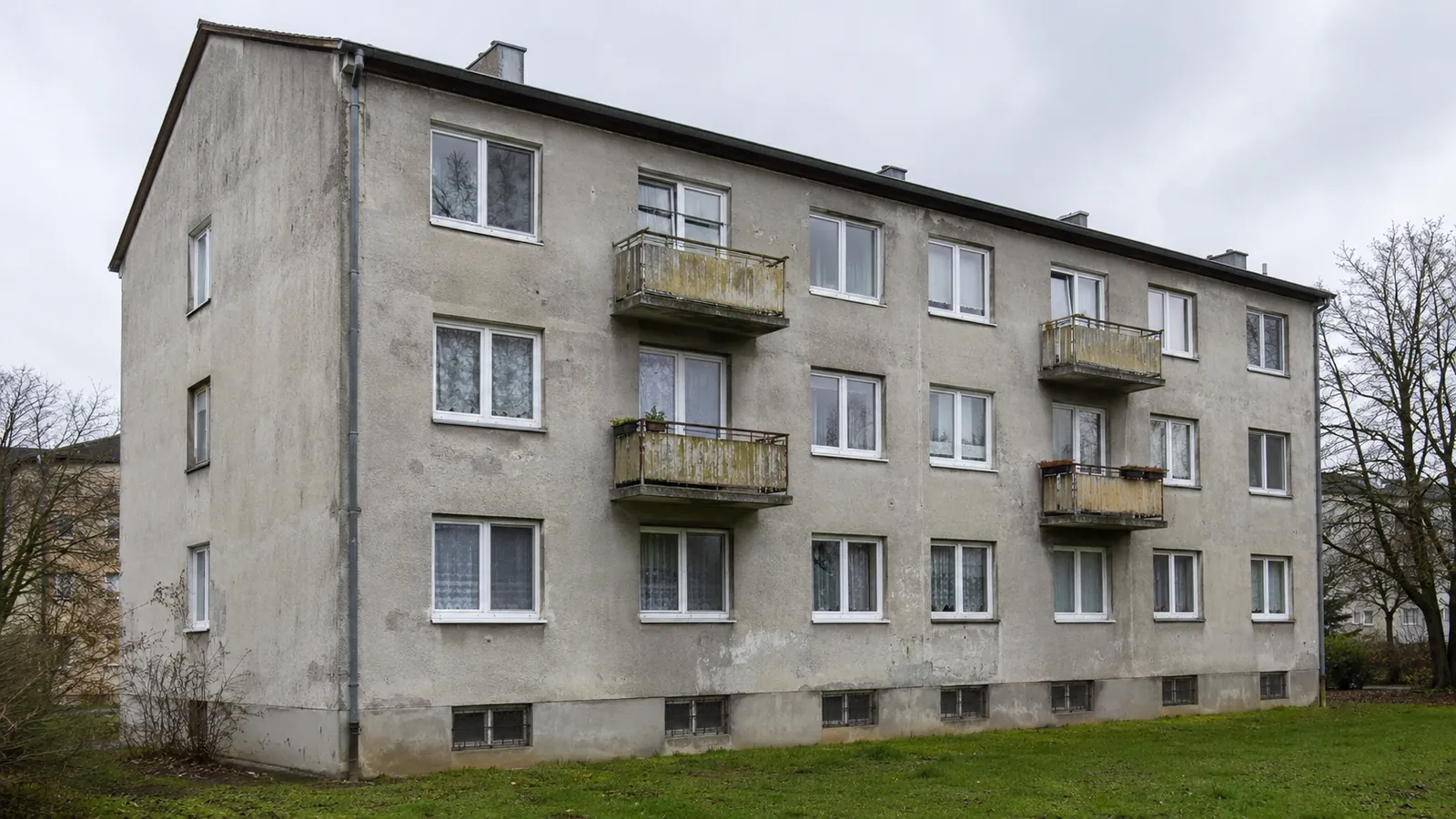 Mehrfamilienhaus aus den 1960er Jahren vor der Sanierung, verwitterter Putz und alte Fenster